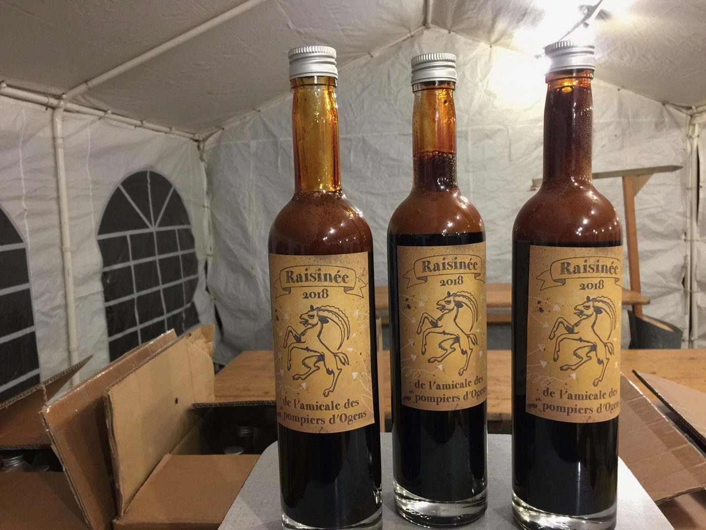 Trois bouteilles de raisinée 2018 étiquetées, posées sur une table sous la tente