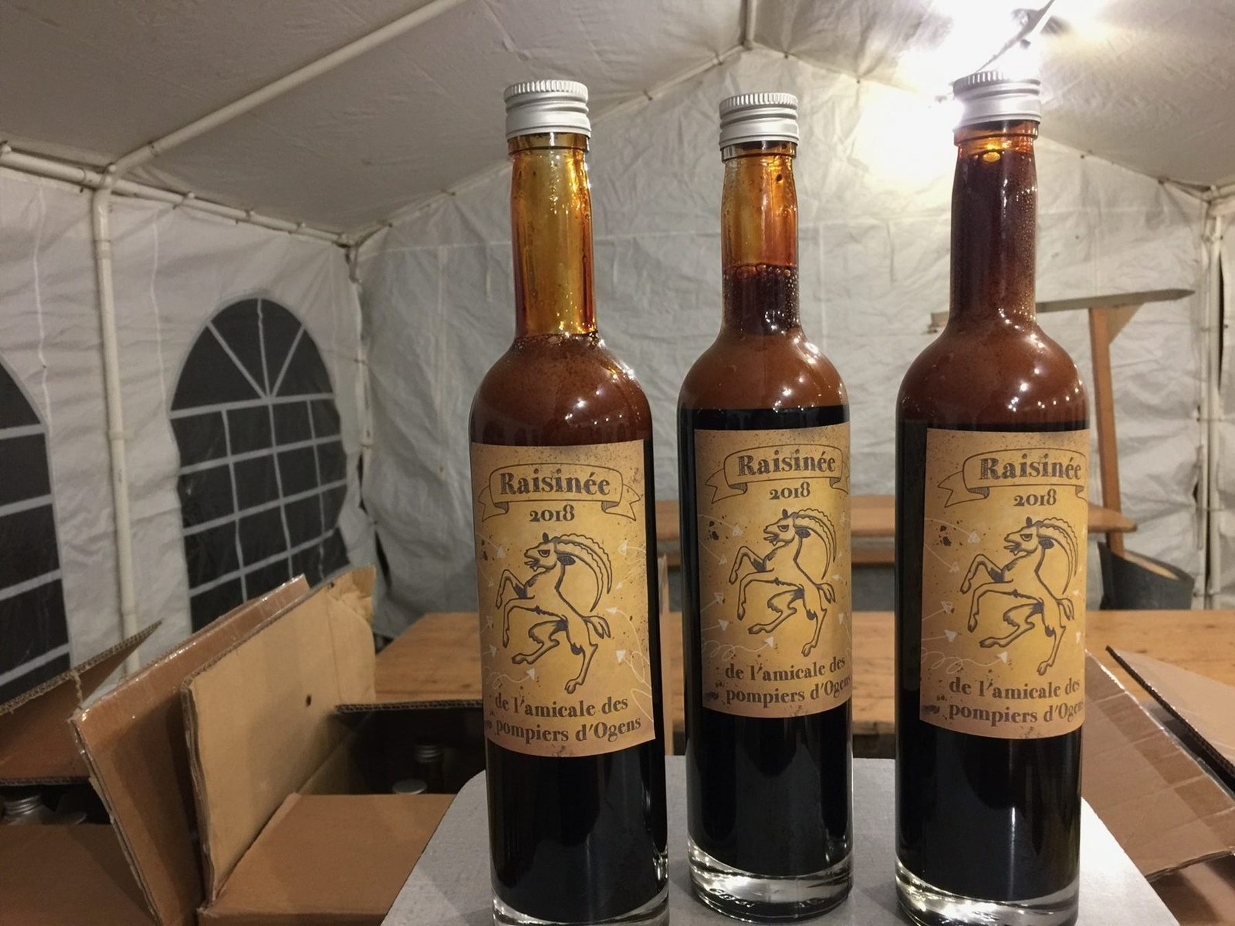 Trois bouteilles de raisinée étiquetées, posées sous la tente