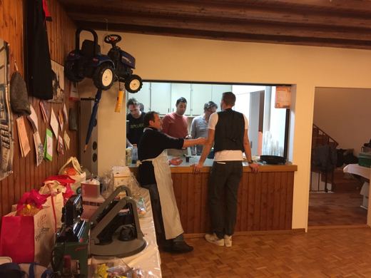 Deux hommes derriere un comptoir de bar improvise dans une salle, un troisieme de face devant eux.