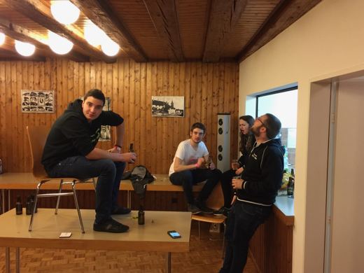 Deux hommes assis face a face a une petite table dans une salle en bois, en pleine conversation.