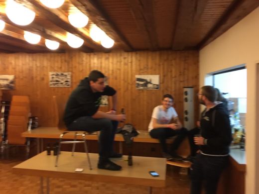 Trois personnes attablees dans une salle boisee, verres a la main, en pleine discussion animee.