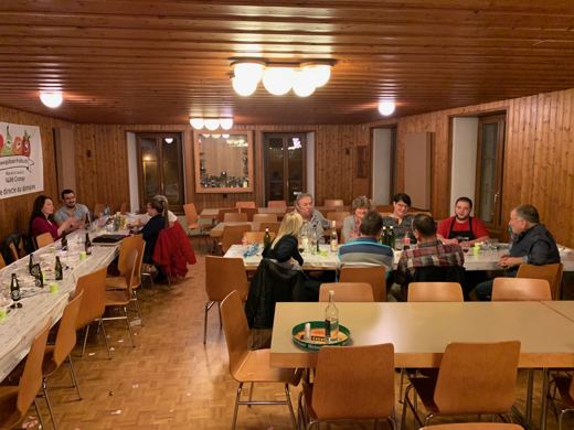 Salle communale avec plusieurs tables occupées par des convives assis, éclairage chaleureux, ambiance de repas de groupe.