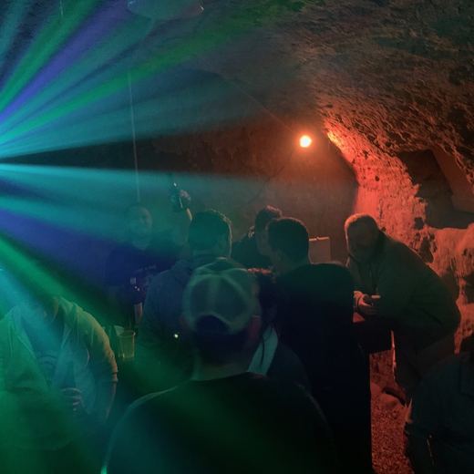 Arche de cave en pierre éclairée de faisceaux de lumière orange et bleue, avec des silhouettes de personnes debout.