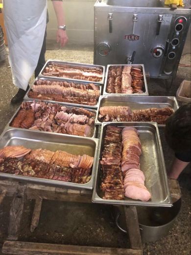 Sept plateaux en inox garnis de lard, de jambon et de saucisses tranchés, devant la marmite de l'ancien abattoir