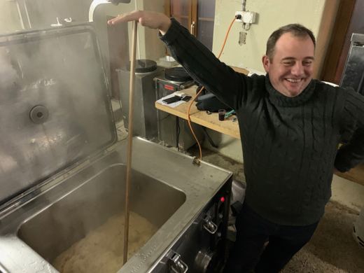 Un membre de l'amicale sourit, le bras tendu au-dessus de la marmite de choucroute fumante