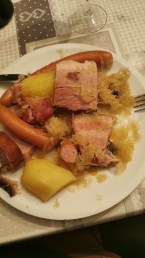 Assiette de choucroute garnie avec deux saucisses, du lard, du jambon et des pommes de terre, sur une nappe grise