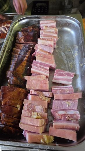 Plateau métallique rempli de tranches de lard et de charcuterie empilées, préparé pour la garniture de la choucroute.