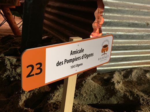 Pancarte orange et blanche portant le numéro 23 et le nom de l'Amicale des Pompiers d'Ogens, de nuit