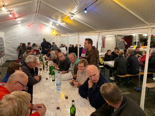 Convives assis autour d'une longue table avec bouteilles et verres sous une tente éclairée de guirlandes colorées