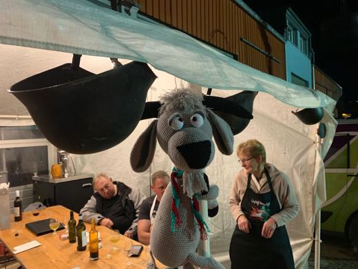 Peluche en forme de mouton suspendue sous une tente, des membres attablés avec des bouteilles en arrière-plan