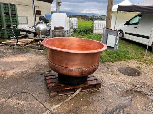 Grand chaudron de cuivre vide posé sur une palette en bois, camionnette blanche et montagnes en arrière-plan