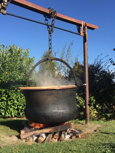 Chaudron noir suspendu à une potence métallique au-dessus d'un feu de bois, ciel bleu dégagé