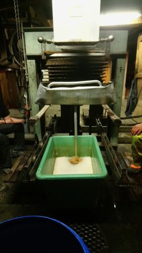 Pressoir métallique dans un atelier de nuit, jus de pomme s'écoulant dans un bac en plastique vert