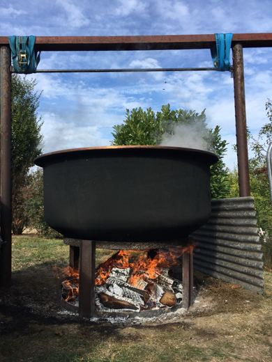 Chaudron noir suspendu à une structure métallique en plein air, léger filet de fumée sous un ciel dégagé