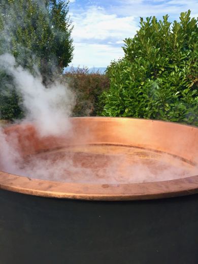 Chaudron de cuivre fumant en gros plan, haies vertes et ciel bleu en arrière-plan