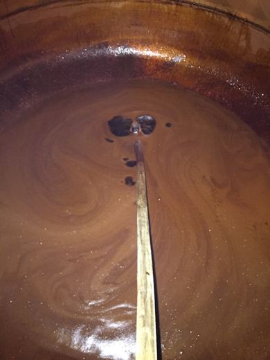 Vue plongeante dans un chaudron de cuivre avec un sirop brun qui tourbillonne autour d'une perche en bois