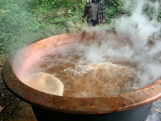 Gros plan sur un chaudron de cuivre en ébullition avec une mousse blanche, un membre en arrière-plan