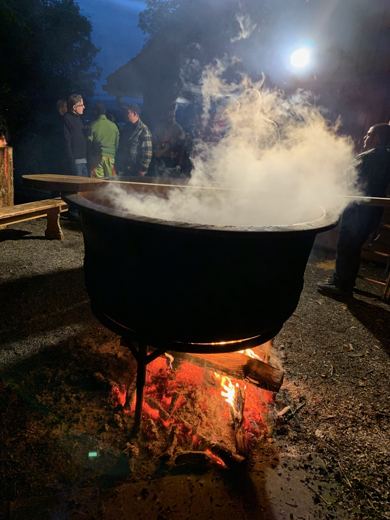Chaudron fumant de nuit, silhouettes de plusieurs personnes rassemblées à l'arrière-plan