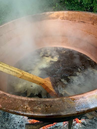 Vue plongeante dans un chaudron de cuivre avec une perche en bois remuant un liquide moussant