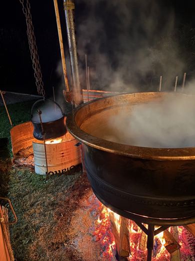 Chaudron de cuivre fumant la nuit au-dessus d'un feu, bidon à lait métallique posé à côté
