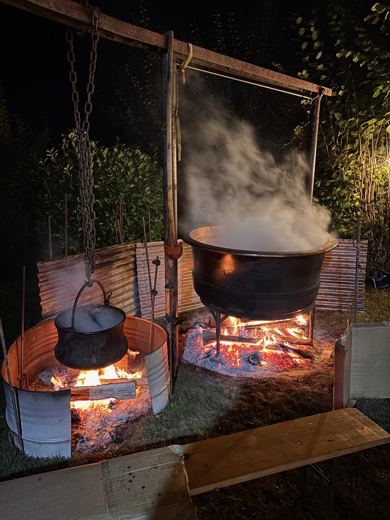 Deux foyers de nuit sous un portique métallique, un petit chaudron et un grand chaudron fumant