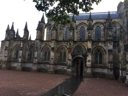 Cour pavée de brique rouge menant à la façade sculptée d'une chapelle gothique en pierre claire.