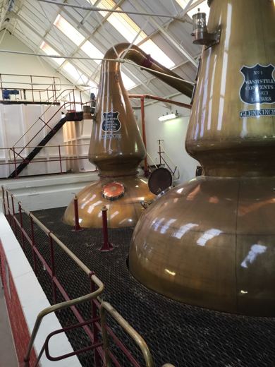 Grands alambics en cuivre poli d'une distillerie de whisky, sous une charpente en bois.