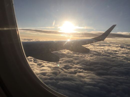 Aile d'avion et mer de nuages illuminées par le soleil levant, vue prise depuis un hublot en vol.