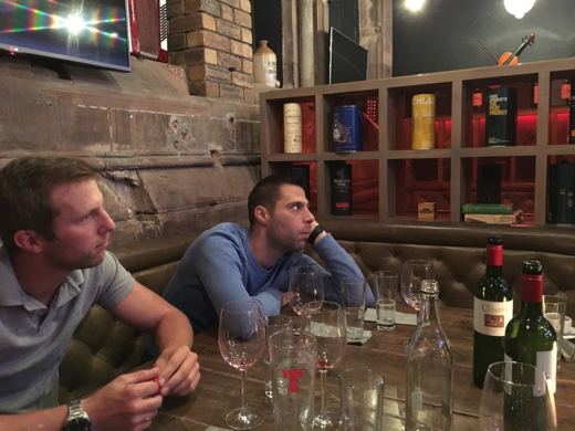 Deux hommes attablés dans un pub, verres posés devant eux, ambiance décontractée.