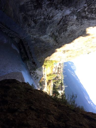 Vue de l'intérieur d'une cave taillée dans la roche, éclairée par la lumière extérieure, montagne visible au loin.