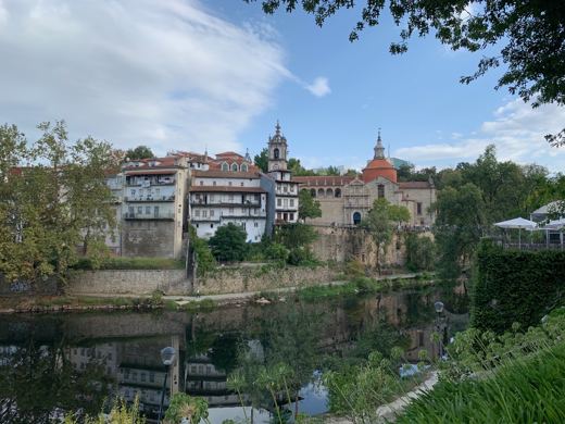 Village portugais en bord de rivière avec bâtiments historiques se reflétant dans l'eau calme, ciel dégagé.