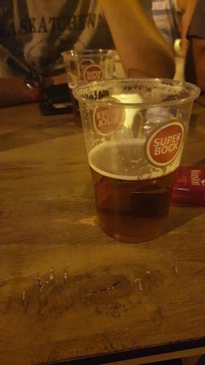 Plusieurs hommes attablés en terrasse avec des chopes de bière, vus de trois quarts à distance modérée.