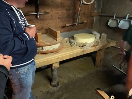 Un homme observe des meules de fromage posées sur une table en bois dans une grange rustique.
