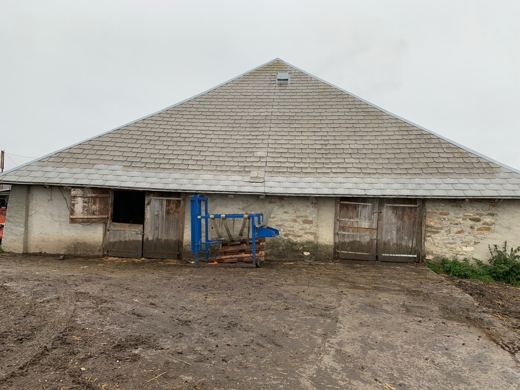 Façade d'un chalet d'alpage traditionnel en pierre et bois, toit de tôle, cour en terre battue.