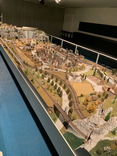 Grande maquette miniature représentant un paysage et un village, exposée derrière une vitre dans un musée.