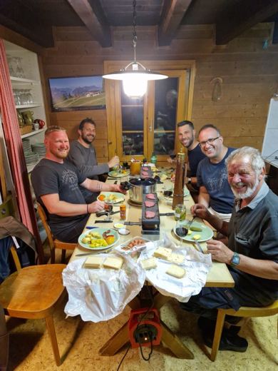 Groupe d'hommes attablés dans un restaurant, verres levés pour un toast, plats et bouteilles sur la table.