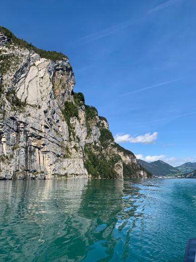 Falaise rocheuse abrupte se reflétant dans une eau turquoise, sillage du bateau au premier plan.