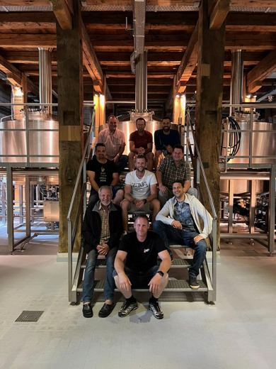 Groupe d'hommes posant sur un escalier en bois entouré de cuves de brasserie en cuivre.