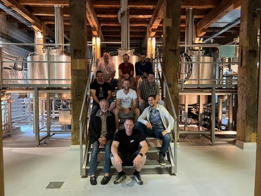 Grand groupe d'hommes posant sur un escalier entouré de cuves de brasserie en inox.