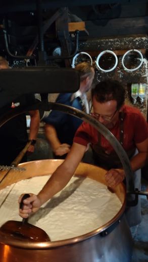 Un homme travaille le caillé dans une grande chaudière de cuivre lors d'une démonstration de fabrication de fromage.
