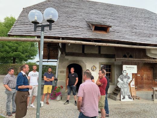 Façade en bois d'un bâtiment rustique de fromagerie, petit groupe de visiteurs rassemblé devant l'entrée.
