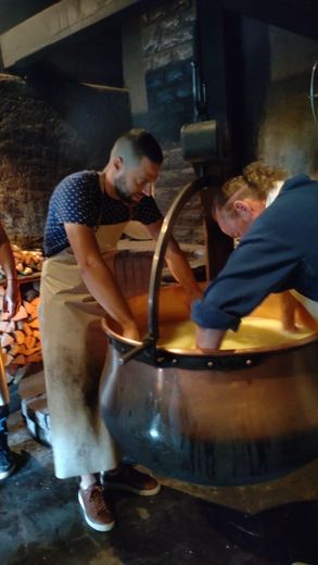 Un homme et une femme travaillent ensemble le fromage dans une chaudière de cuivre, ambiance conviviale.