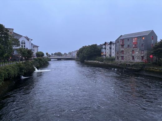 Canal traversant une ville irlandaise bordée de façades colorées, lumière douce du soir, ciel voilé.