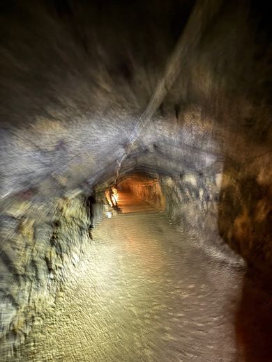 Vue en perspective d'une galerie de mine d'asphalte éclairée, tunnel voûté se prolongeant dans la pénombre.