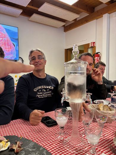 Groupe d'hommes attablés autour d'une carafe d'absinthe, nappe à carreaux et verres à absinthe sur la table.