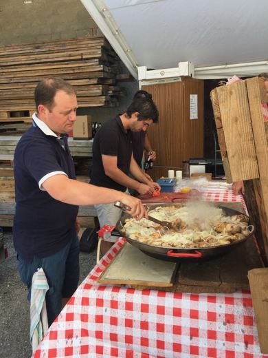 Un homme mélange le contenu d'une grande poêle fumante avec une spatule, un second homme regarde à côté.