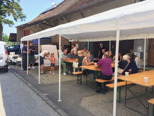 Vue d'ensemble d'une tente blanche dressée dans une rue de village, avec des tables où des personnes sont attablées.