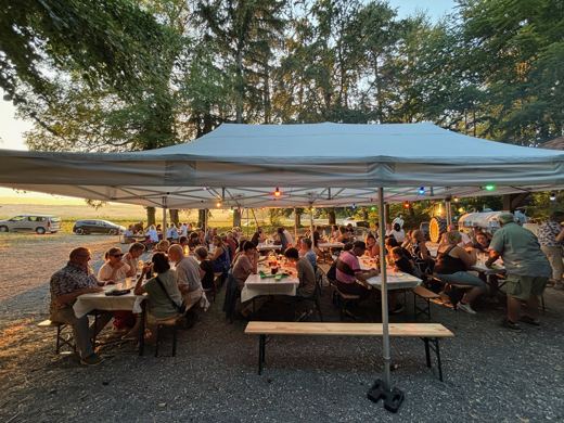 Vue large de la tente du 1er août, les tables et les bancs pleins, les arbres derrière