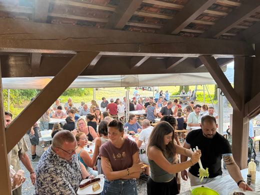 Des convives se servent au buffet sous le toit en bois du refuge, la foule attablée derrière